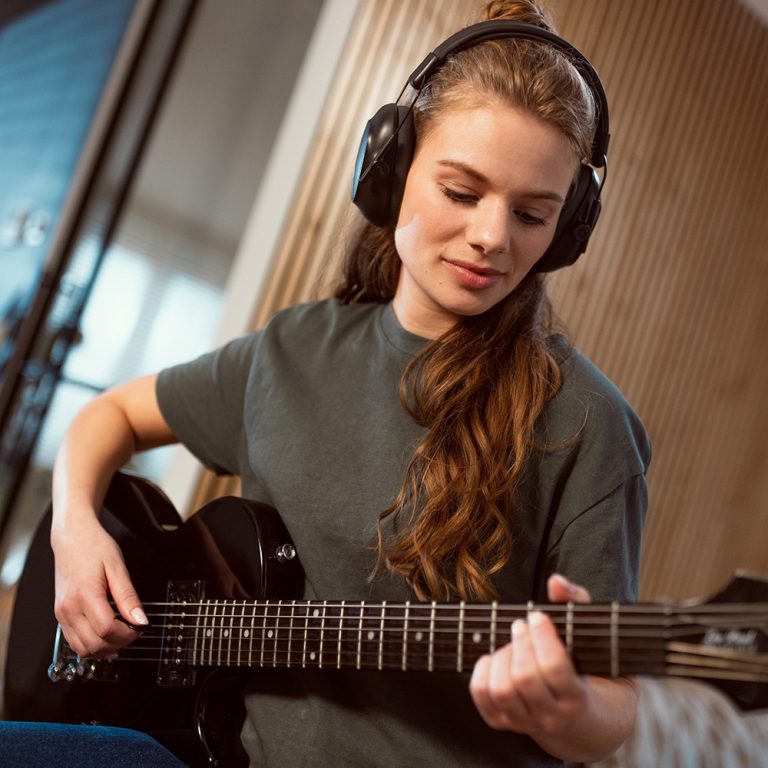 Girl playing guitar wearing Alpine Defender Ear Protection for Adults and Teens
